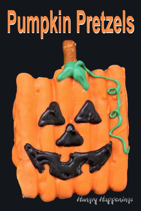 orange chocolate dipped pretzels arranged into a square decorated like a jack-o-lantern sitting on a black background