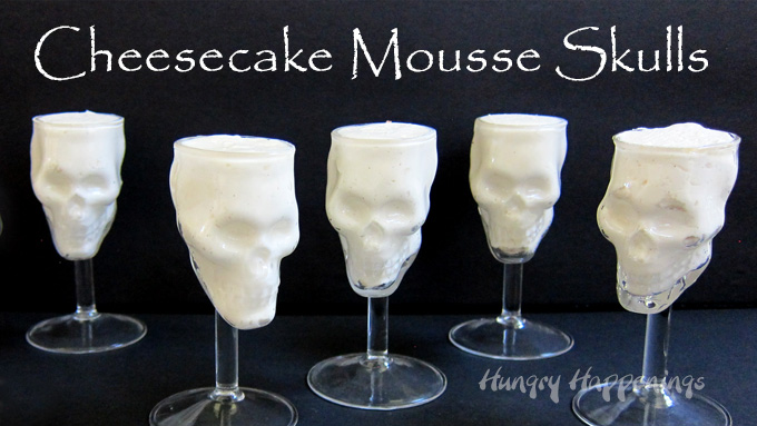 5 skull shaped glasses filled with cheesecake mousse on a black background