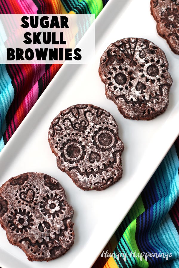 Sugar skull brownies dusted with powdered sugar are arranged on a long white plate set on a colorful poncho.