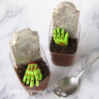 two chocolate mousse graveyards with green candy zombie hands and cookies and cream candy bar tombstones