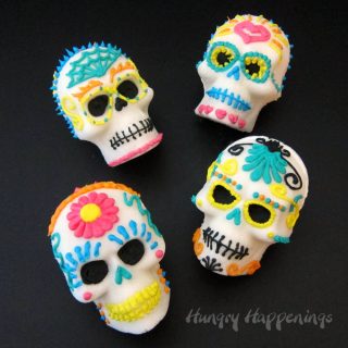 four sugar skulls decorated with colorful royal icing flowers, hearts, spider webs and more on a black background