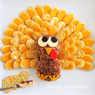 bacon ranch cheese ball decorated to look like a turkey is surrounded by cheese topped cracker feathers