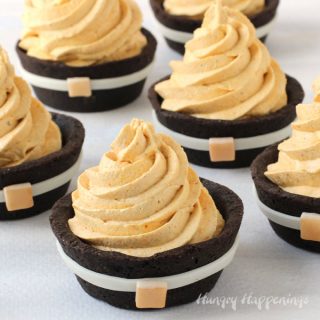 chocolate cookie cups decorated to look like pilgrim suits are filled with pumpkin cheesecake mousse