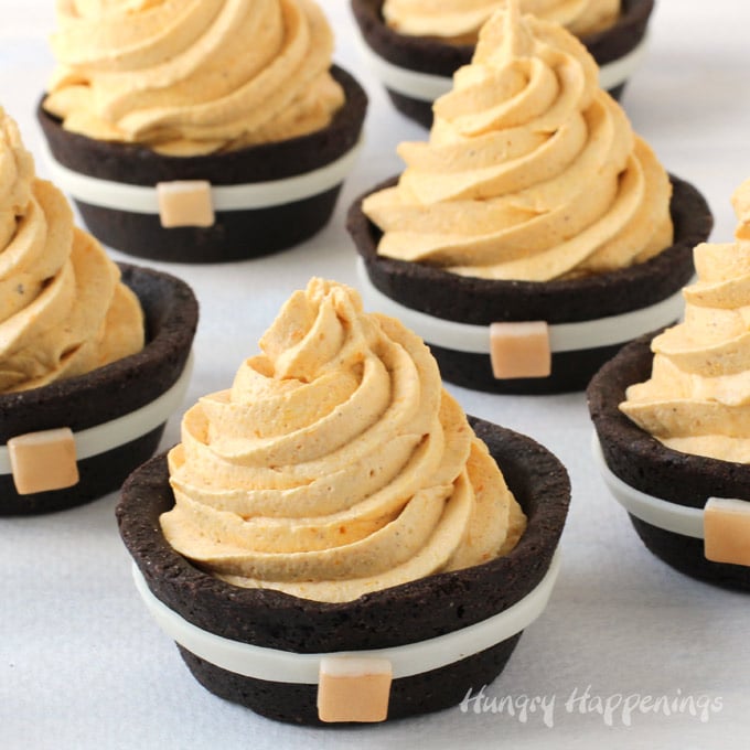 chocolate cookie cups decorated to look like pilgrim suits are filled with pumpkin cheesecake mousse