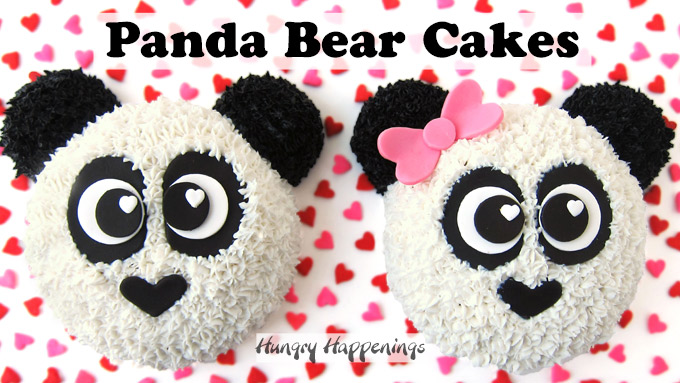 a cute pair of panda bear cakes, one girl panda with a pink bow, the other boy panda without, are sitting next to each other on a white cake board covered in red and pink jumbo heart sprinkles