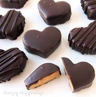 Chocolate Peanut Butter Hearts on a white background. The heart at the bottom of the picture is cut open revealing the peanut butter fudge inside a chocolate shell.