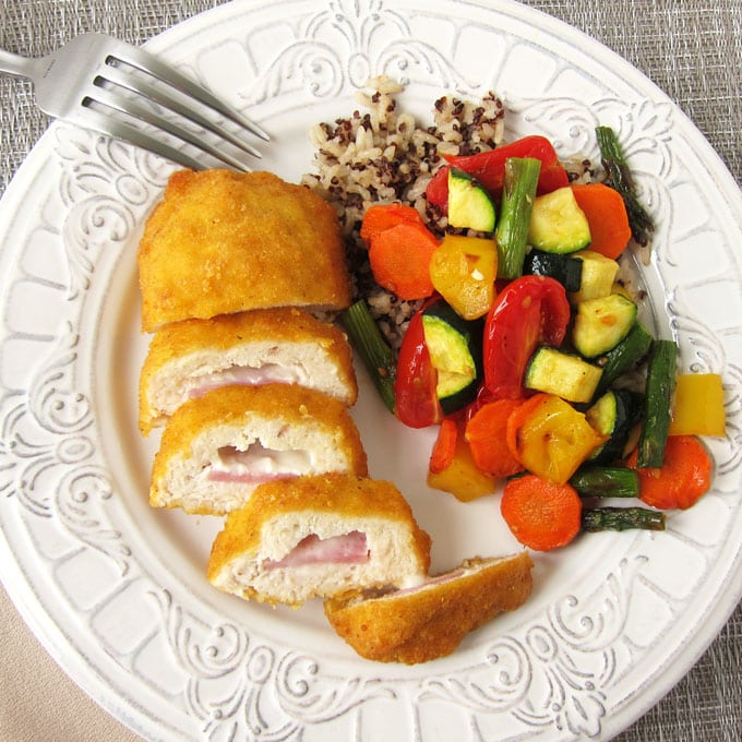Barber Foods Cordon Bleu Stuffed Chicken Breasts cut open and served on a white plate alongside air fried vegetables and a blend of quinoa and rice. 