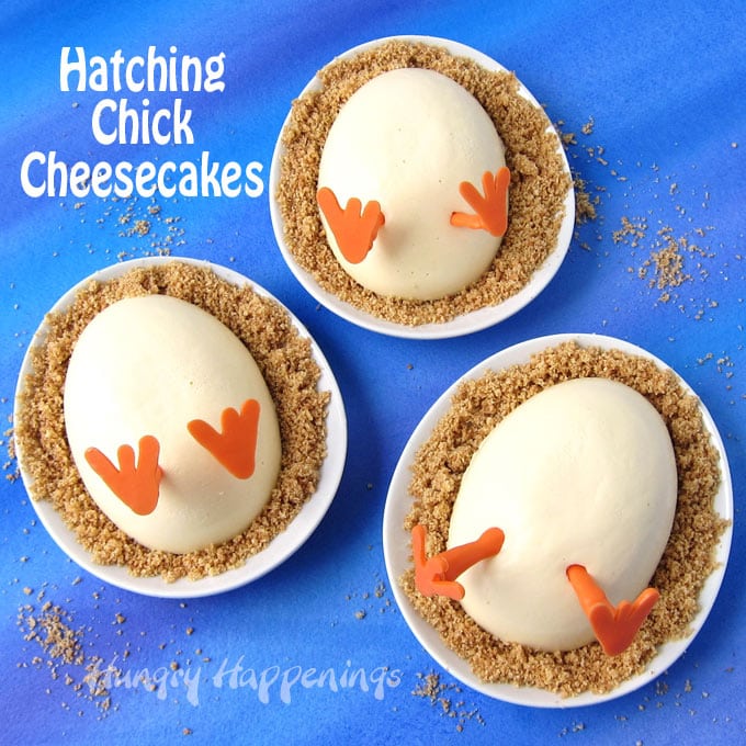 3 oval plates topped with hatching chick cheesecakes served on graham cracker crumbs on a blue watercolor background