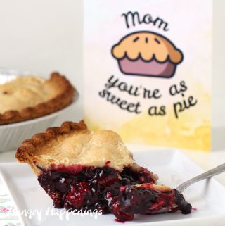 a slice of Sara Lee Wildberry Pie with Zesty Lemon Crust sitting on a square white plate in front of the pie and a "Mom, you're as sweet as pie" card
