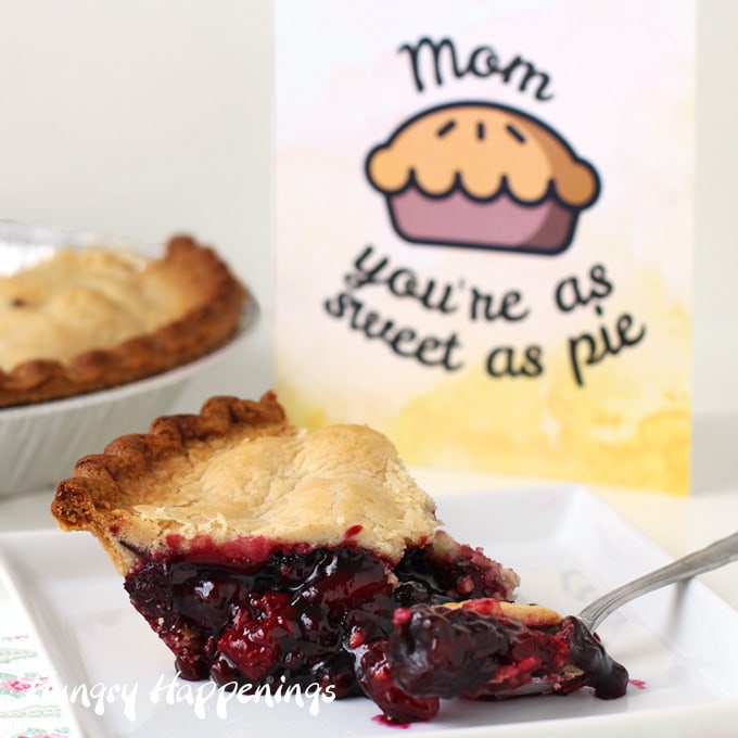 a slice of Sara Lee Wildberry Pie with Zesty Lemon Crust sitting on a square white plate in front of the pie and a 