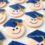cute graduation cookies decorated with modeling chocolate smiley faces and blue candy clay grad caps with gold tassels