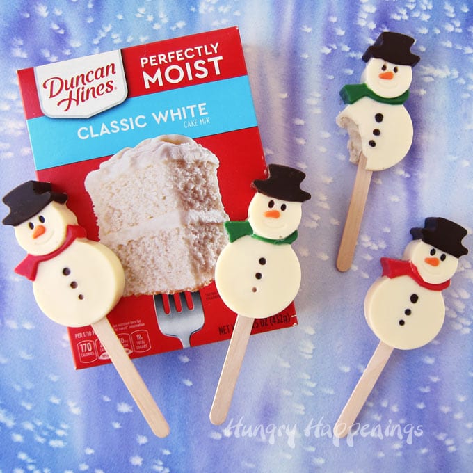 Snowman Cakesicles arranged on a  box of Duncan Hines Cake Mix on a snowy blue background