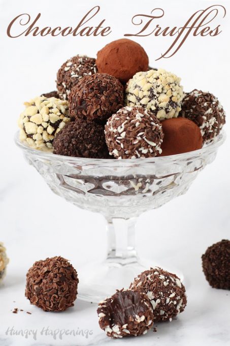 Beautifully chocolate truffles coated in chocolate shavings, cocoa powder, chopped nuts, and cookie crumbs are piled high in a glass candy dish.