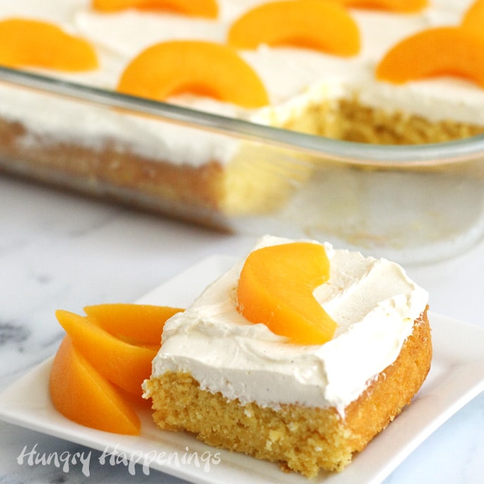 Slice of peach cake topped with cream cheese frosting and a slice of peach is set in front of the sheet cake. 