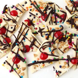 white chocolate ice cream sundae bark topped with maraschino cherries, peanuts, sprinkles, and chocolate ganache