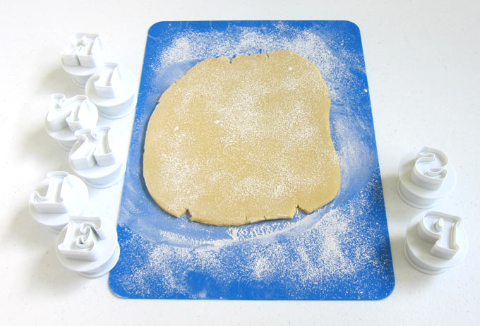 sugar cookie dough rolled out on a silicone mat will be cut using alphabet plunger cutters