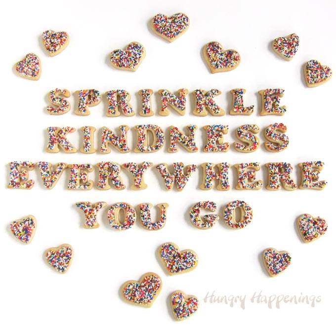 "Sprinkle Kindness Everywhere You Go" cut-out cookies decorated with white candy melts and nonpareils surrounded by heart-shaped sprinkle cookies.