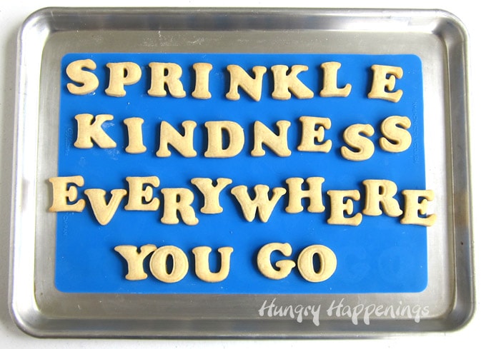 "Sprinkle Kindness Everywhere You Go" cookies on a blue silicone made set on a baking sheet. 