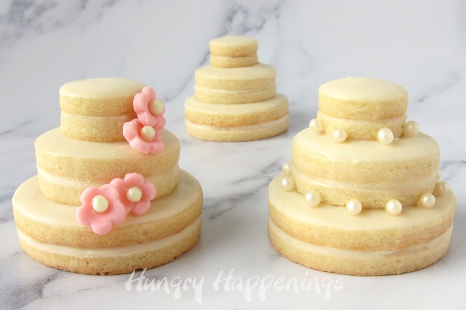 Round cookies stacked on top of each other to create mini wedding cakes are decorated with fondant flowers or sugar pearls. 