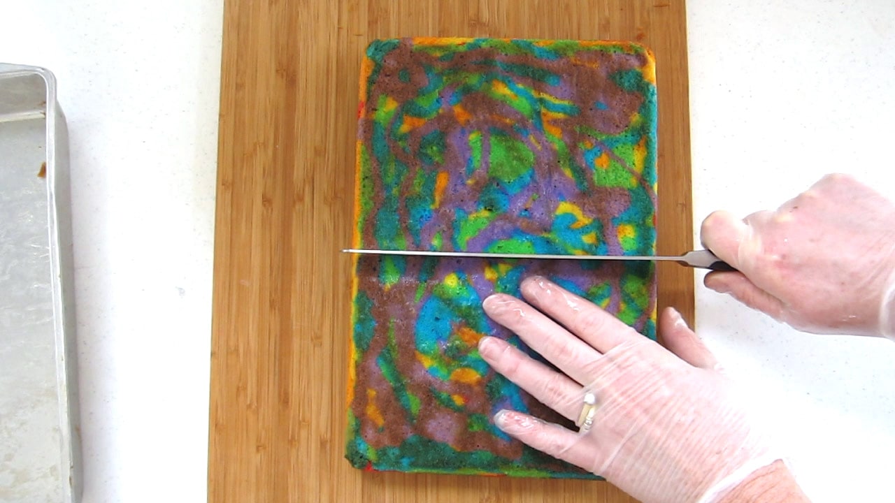 cutting rainbow tie-dye cake in half.