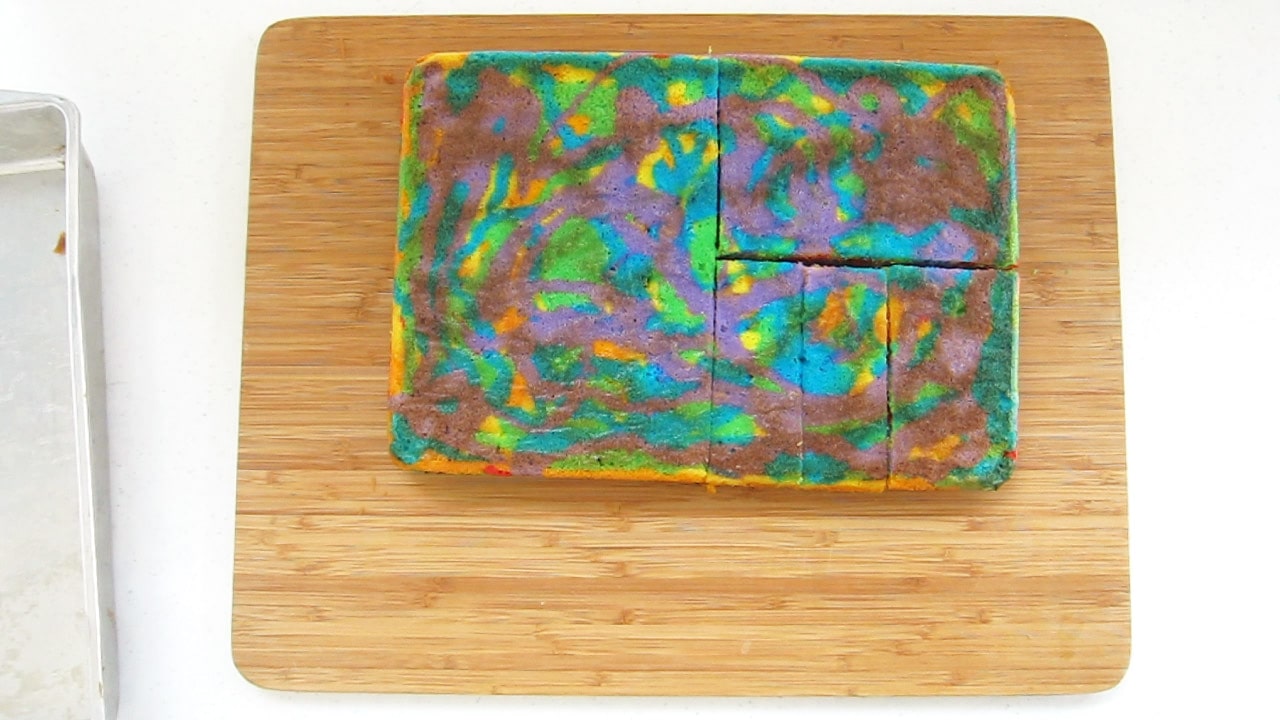 rainbow cake cut in half, then one half is cut in half again, and one half of that is cut into three thin rectangles. 