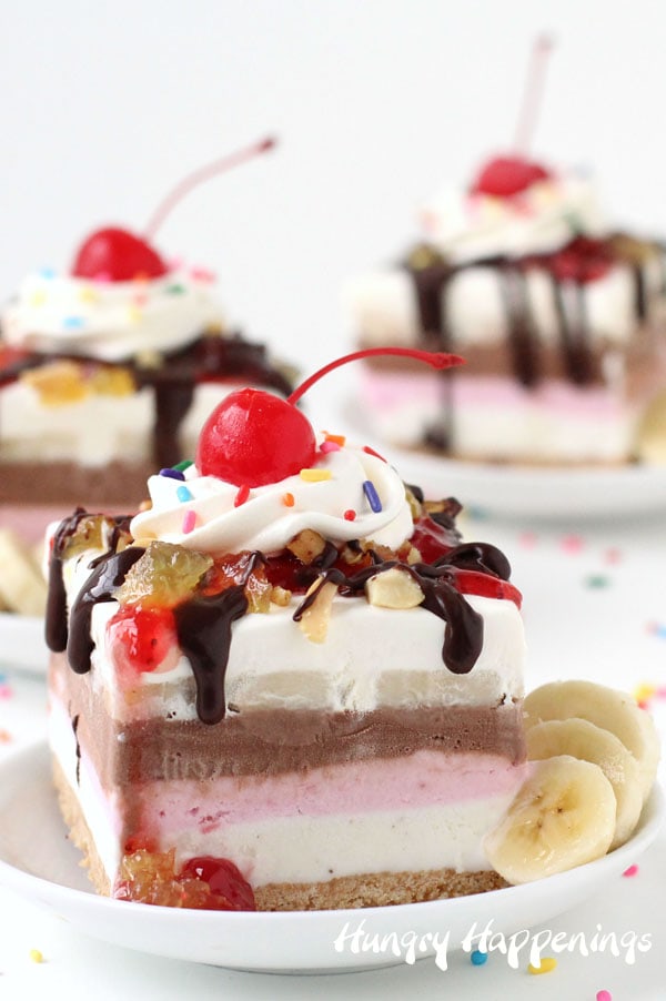 3 banana split bars with layers of vanilla, chocolate, and strawberry ice cream topped with whipped cream chocolate, pineapple, and strawberry sauce are served on white round plates with extra banana slices
