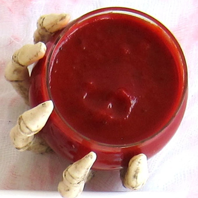blood red marinara sauce served in a clear bowl held by a skeleton hand