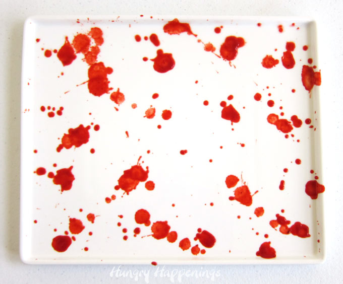 splatter red-colored, thinned pizza sauce onto a white platter to create a blood-stained appearance