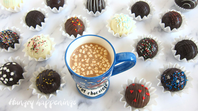 A mug of hot cocoa surrounded by milk, dark, and white chocolate hot cocoa bombs. 