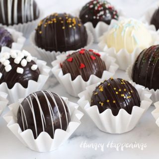 Assorted hot chocolate bombs made using dark, milk, and white chocolate are decorated with sprinkles, marshmallows, and edible glitter.
