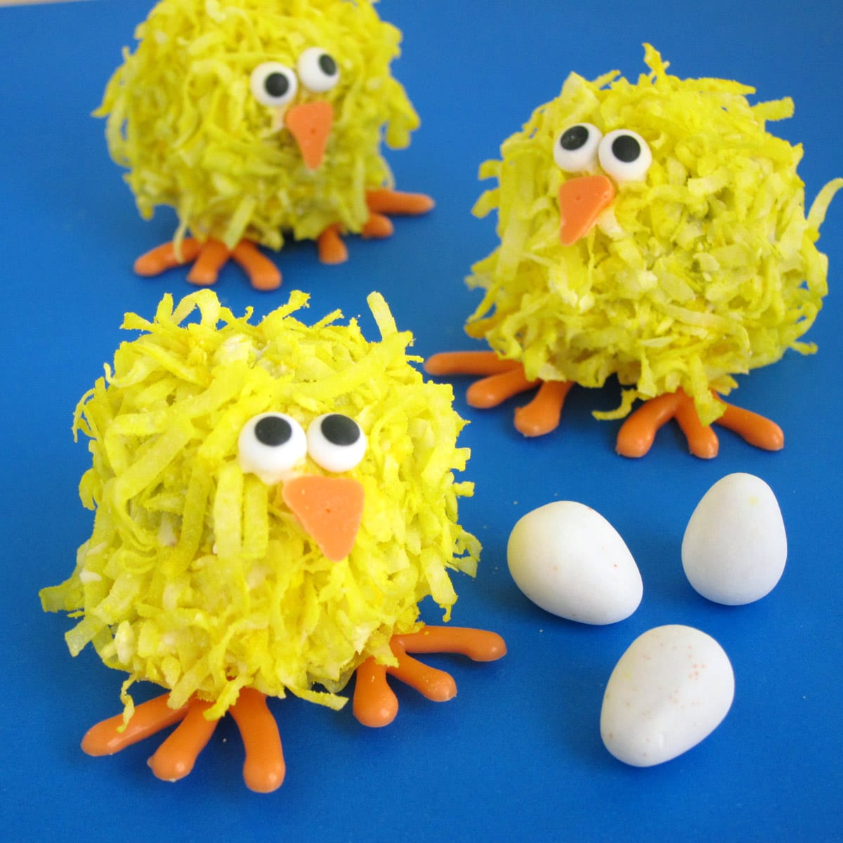 coconut cake ball chicks next to candy eggs on a blue background