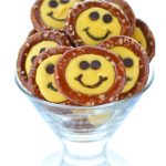 Smiley Face Pretzels - yellow-colored candy melt circles inside pretzel rings with chocolate chip eyes and a black food coloring smile
