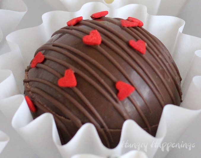 Milk chocolate hot chocolate bombs decorated for Valentine's Day using red heart sprinkles.