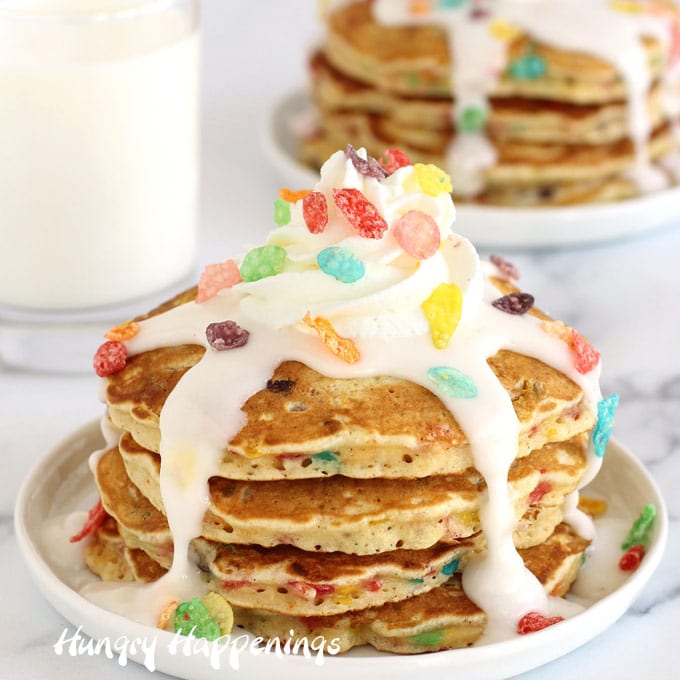 Cereal and Milk Pancakes made with Fruity Pebbles are topped with milk glaze and whipped cream.