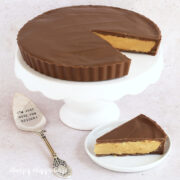 Giant Reese's Cup on a cake stand with a slice cut and served on a small dessert plate.