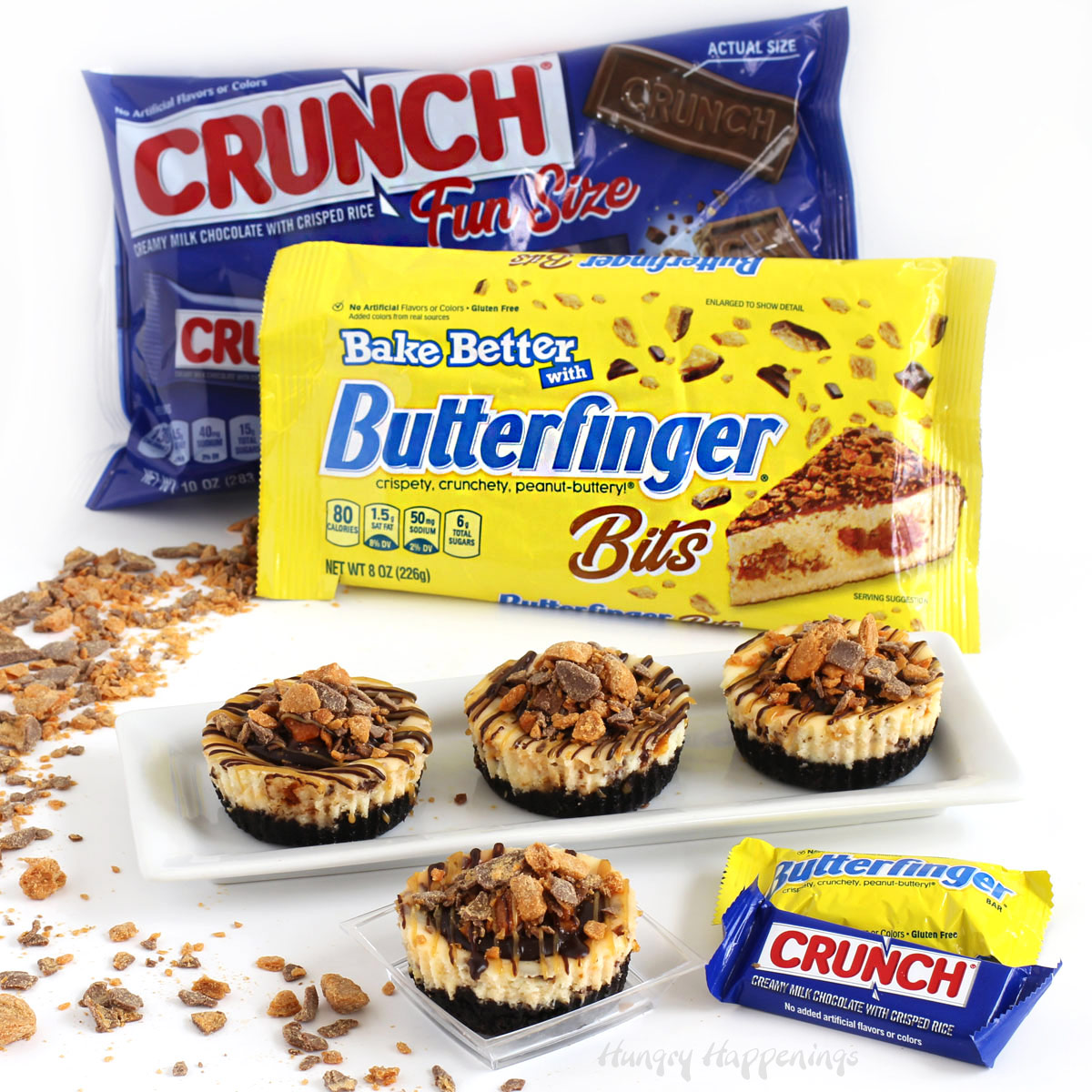 Mini Butter finger Cheesecakes drizzled with chocolate ganache and peanut butter displayed with Nestle Crunch bars and Butterfinger Bars.