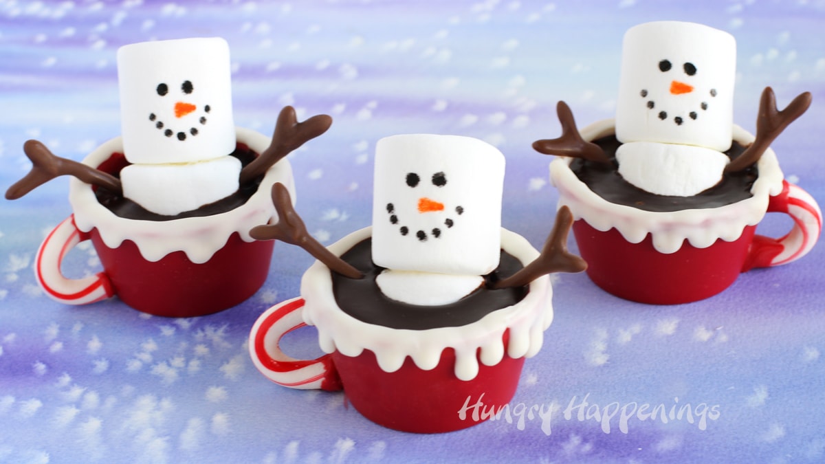 Christmas Hot Chocolate Bombs - 3 marshmallow snowmen in red candy cups with candy cane handles and chocolate ganache filling.