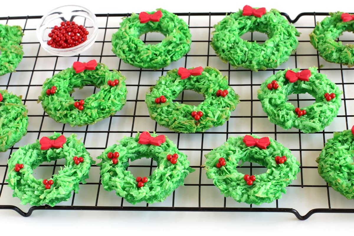 Green coconut macaroon cookie wreaths topped with red sugar pearls and modeling chocolate bows. 