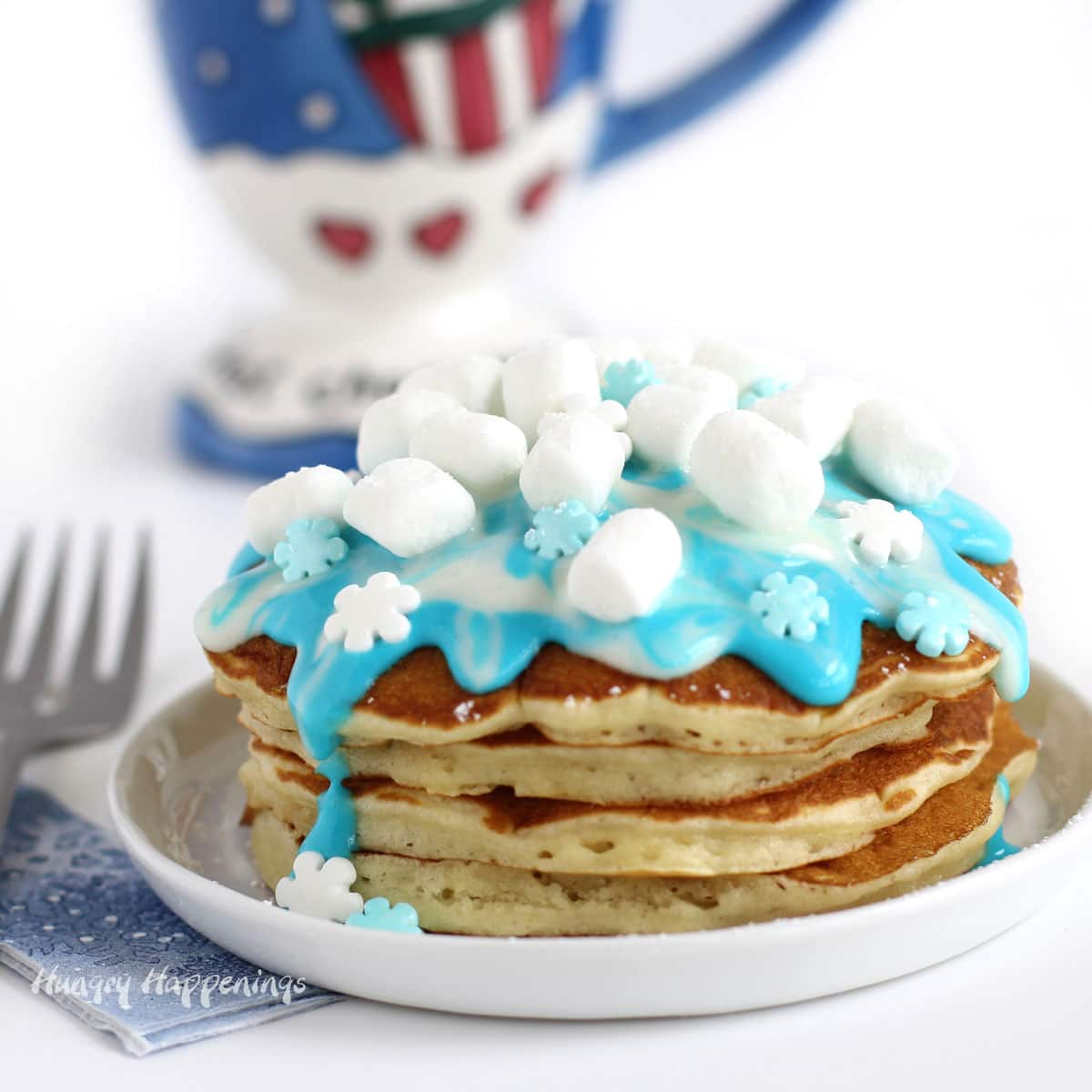 Copycat IHop Winter Wonderland Pancakes topped with blue and white swirled icing, mini marshmallows, and candy snowflakes.