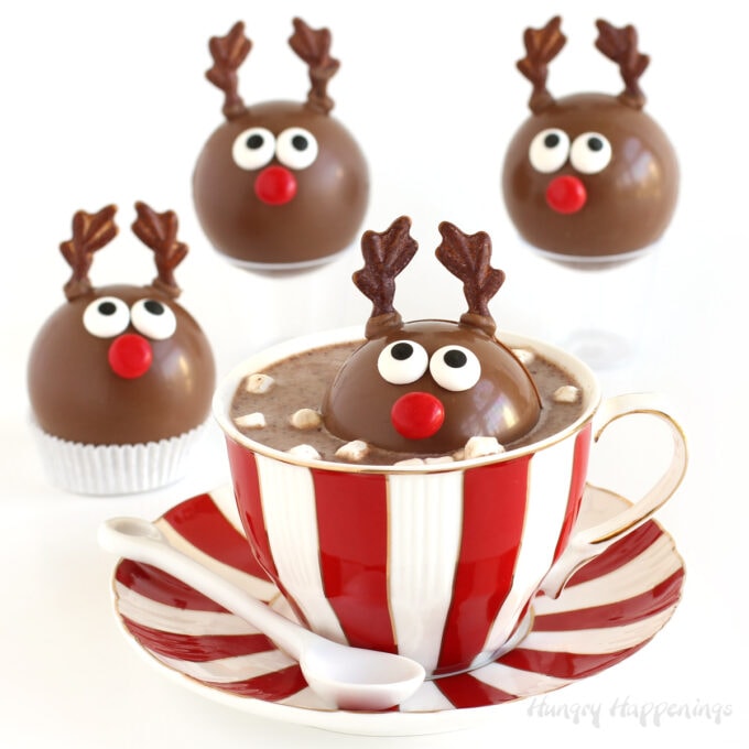 Reindeer Hot Cocoa Bombs with one melting in a mug of hot milk and three surrounding the mug.