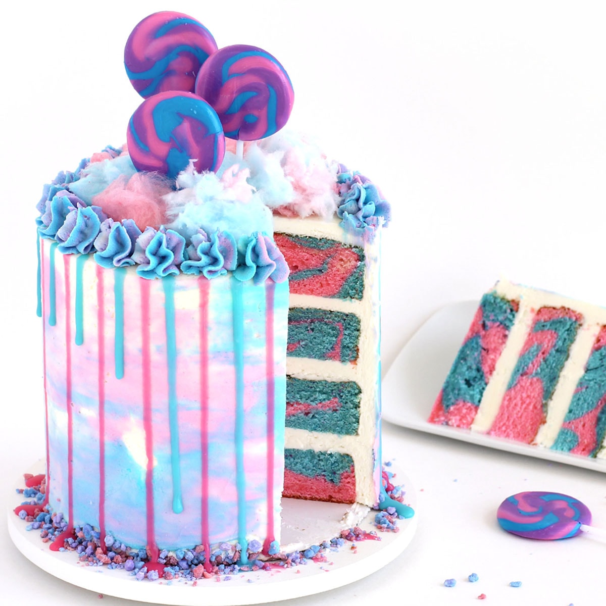 Pink and blue swirled cotton candy layer cake topped with drips of pink and blue ganache and fluffy cotton candy.