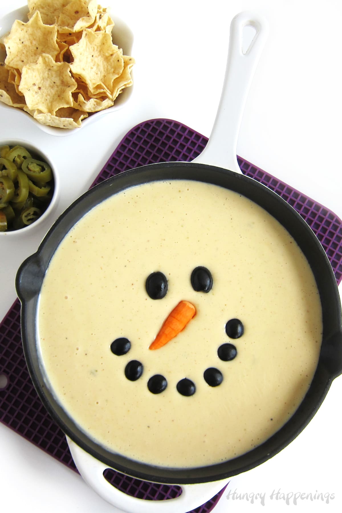 White queso dip snowman served in a skillet with tortilla chips and jalapenos