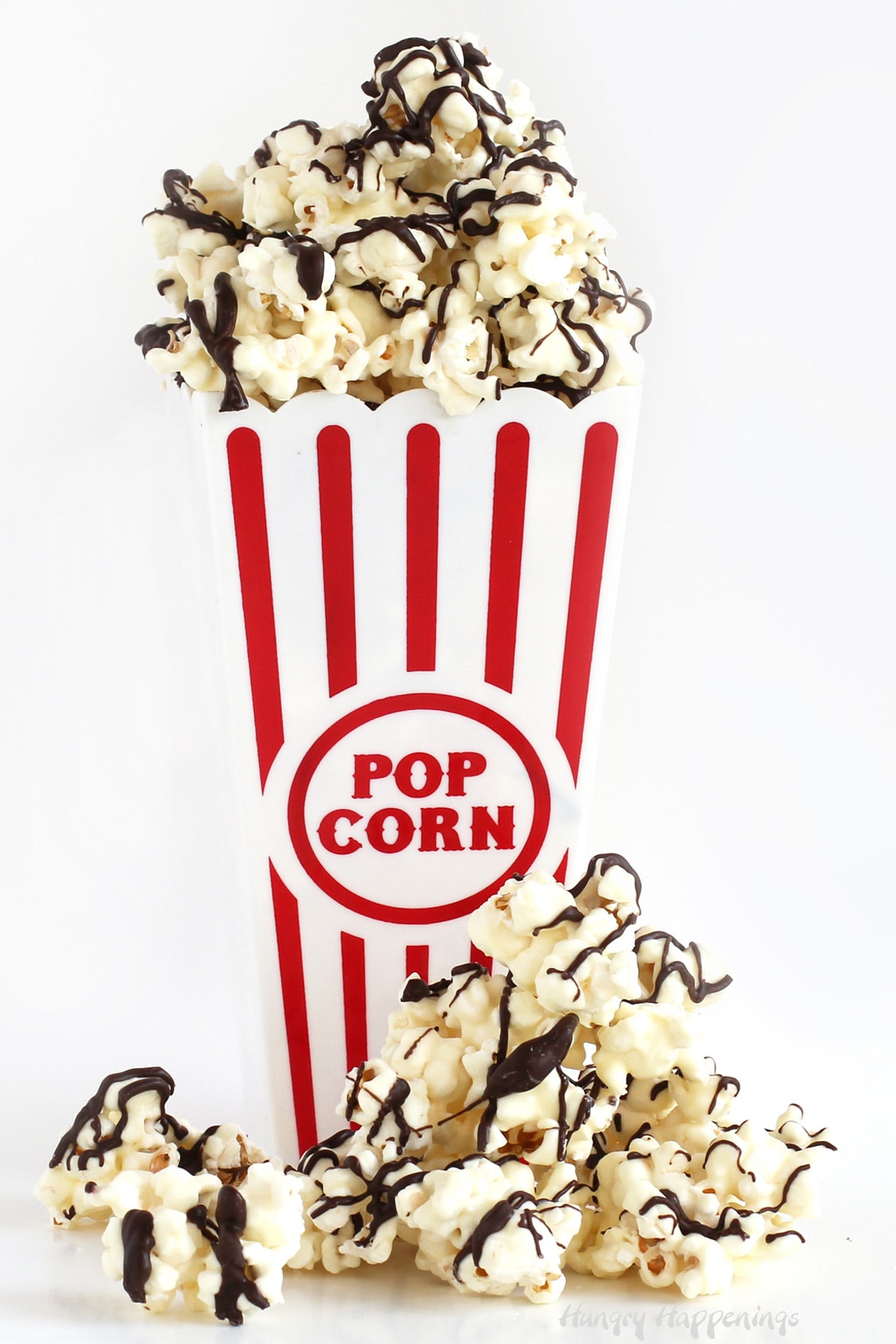 Chocolate popcorn in a red and white striped popcorn box is coated in white chocolate and drizzled with dark chocolate.