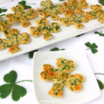 shamrock cracker crisps topped with chopped parsley set on a white plate on a St. Patrick's Day kitchen towel
