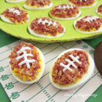 Deviled egg footballs decorated with bacon and mayonnaise laces set in a egg serving platter