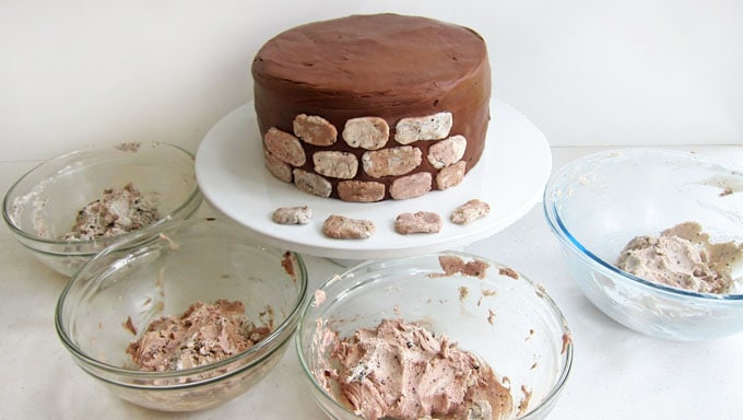 chocolate frosted cake decorated with cookies and cream fudge stones surrounded by bowls of fudge