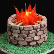 s'mores camp fire cake decorated with cookies and cream fudge stones, cookie sticks, and candy flames