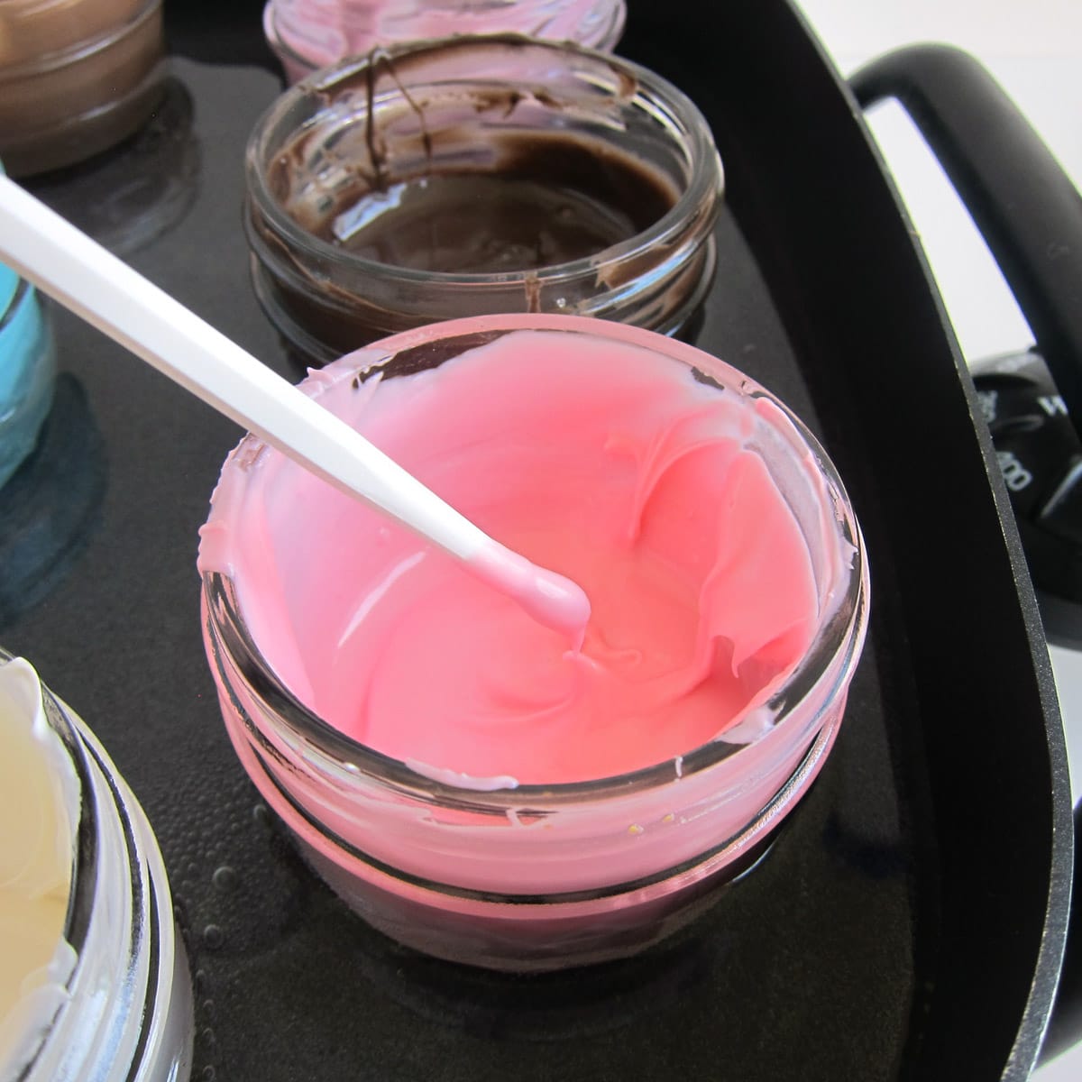 Dip a paint brush into melted pink candy melts that are in a jar in a water bath in an electric skillet.