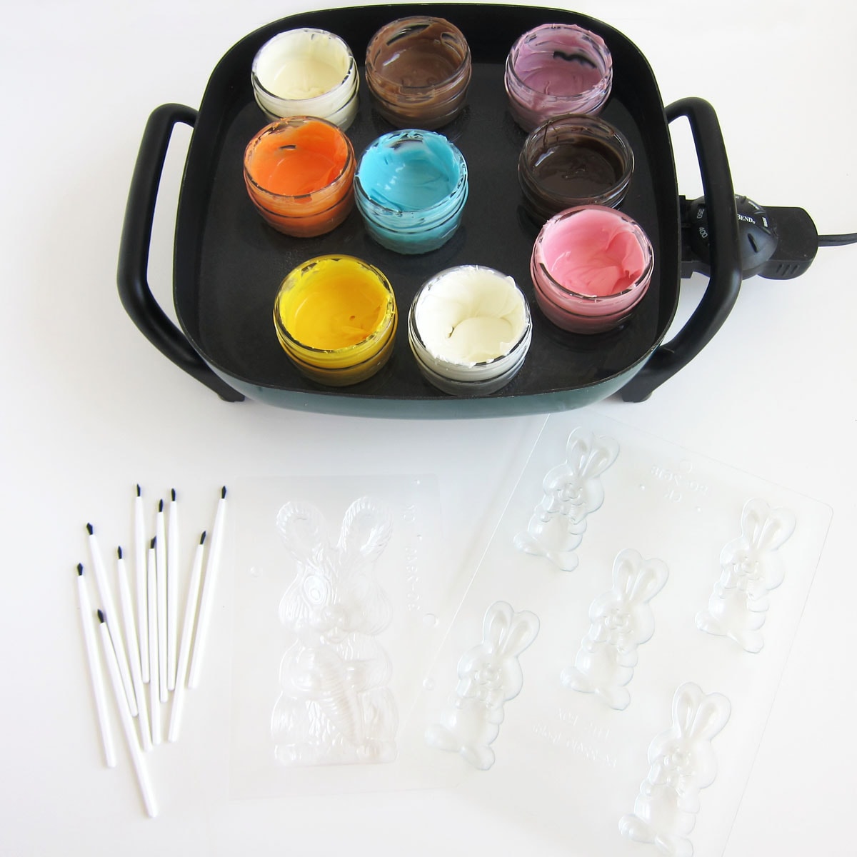 Melting candy melts in a water bath in an electric skillet sitting next to paint brushes and candy molds.