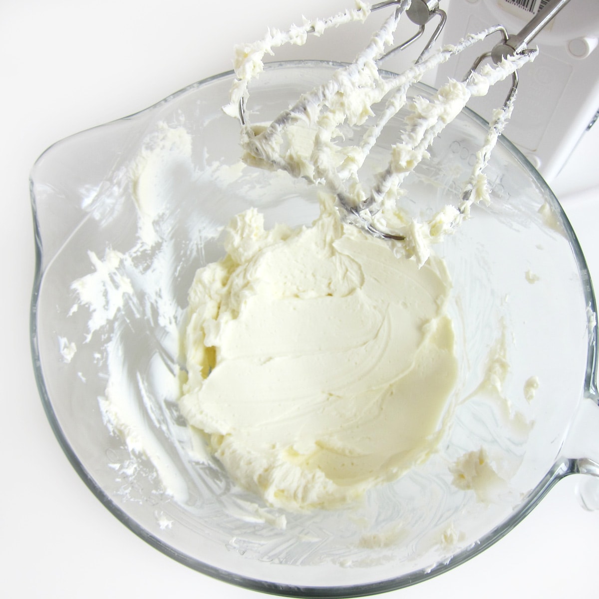 Cream cheese in a mixing bowl is creamed using a hand-held mixer.
